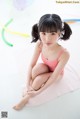 A little girl in a pink bathing suit sitting on a pink towel.