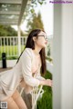 A woman wearing glasses leaning against a white chair.