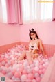 A woman sitting in a bathtub filled with pink and white balls.