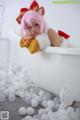 A woman with pink hair laying in a bathtub filled with white balls.