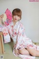 A woman in a kimono sitting on the floor holding a fan.