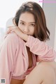 A woman in a pink robe sitting on a bed.