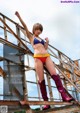 A woman in a bikini and boots posing on a metal structure.