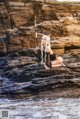 A woman sitting on a rock by the water holding a spear.