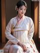 A woman in a white hanbok sitting on a window sill.